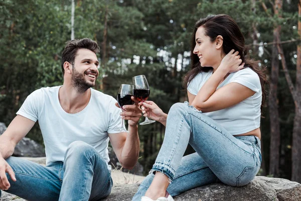 Alegre hombre y joven mujer tintineo copas de vino en el bosque - foto de stock