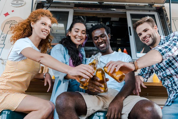 Amigos multiculturales felices tintineo botellas con cerveza cerca de camión de comida - foto de stock