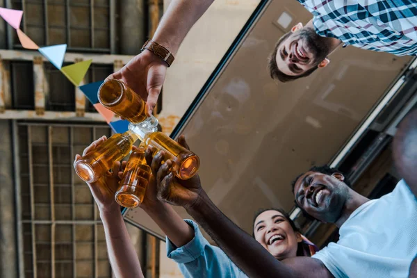 Bottom view of happy multicultural friends toasting bottles with beer — Stock Photo