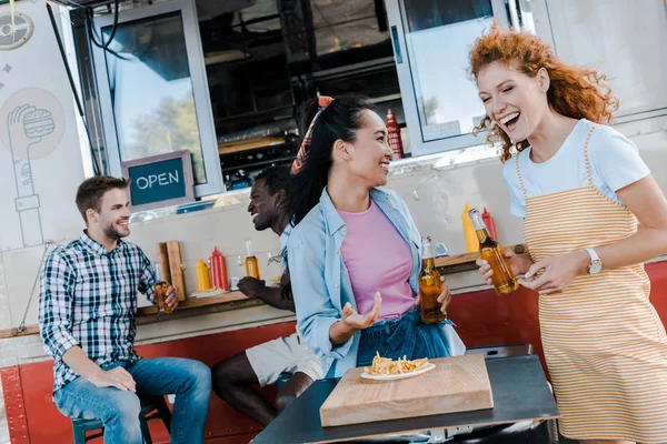 Filles heureuses riant près des hommes multiculturels et camion de nourriture — Photo de stock