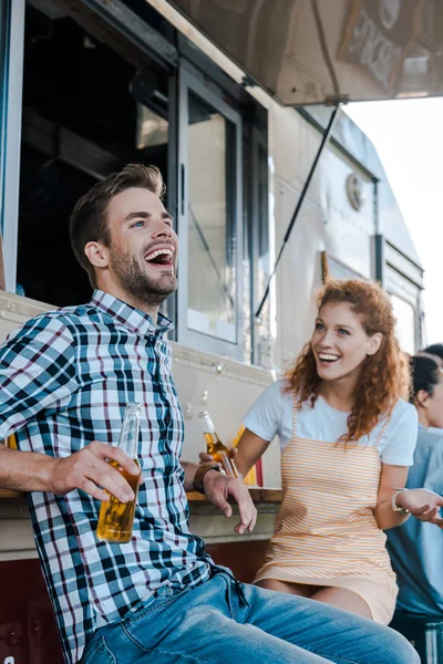 Selektiver Fokus eines glücklichen Mannes, der neben einem rothaarigen Mädchen in der Nähe eines Foodtrucks lacht — Stockfoto