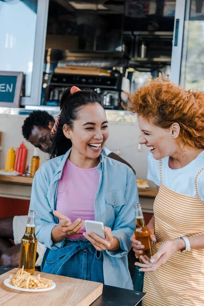 Selective focus of multicultural girls laughing near african american man and food truck — Stock Photo