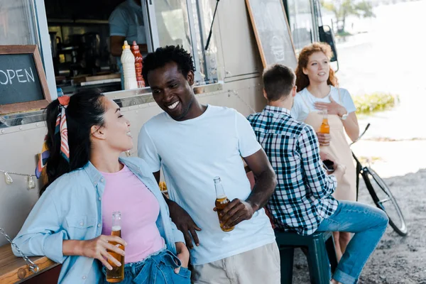 Enfoque selectivo de africano americano hombre mirando asiático chica cerca de comida camión - foto de stock