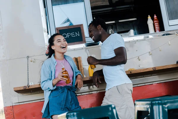 Felice ragazza asiatica ridere vicino afro americano uomo con bottiglia di birra — Foto stock