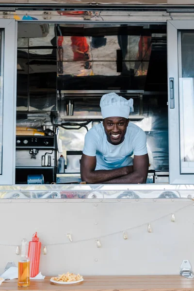 Счастливый африканский американец в форме шеф-повара, улыбающийся от грузовика с едой — стоковое фото