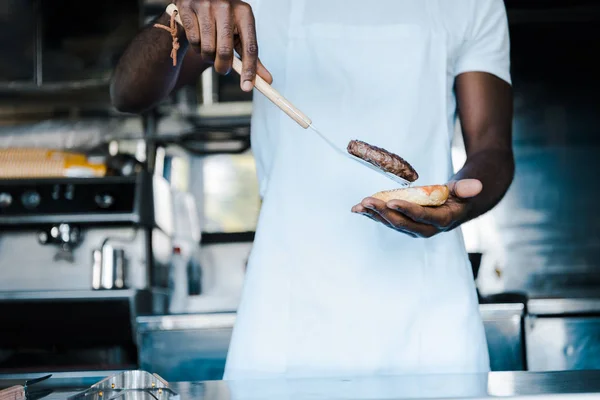 Vista recortada del hombre afriano americano sosteniendo espátula mientras prepara hamburguesa - foto de stock