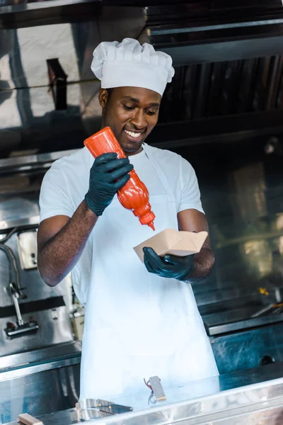 Веселий афроамериканський чоловік тримає пляшку кетчупу біля картонної пластини — стокове фото
