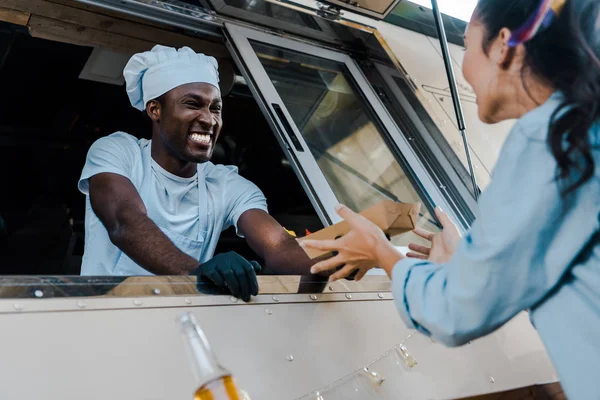 Vue à faible angle de l'homme afro-américain joyeux donnant la plaque de carton au client — Photo de stock