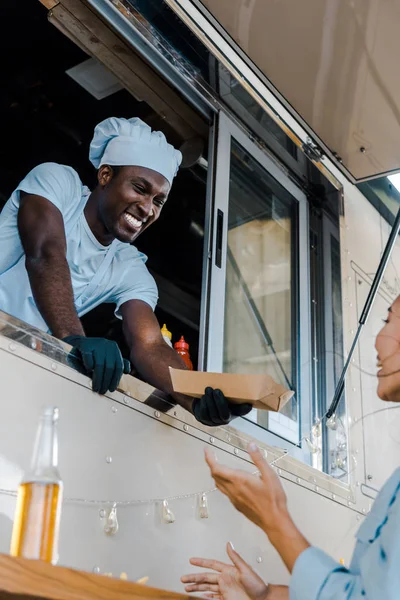 Low angle view of happy african american man giving carton plate to asian customer — Stock Photo