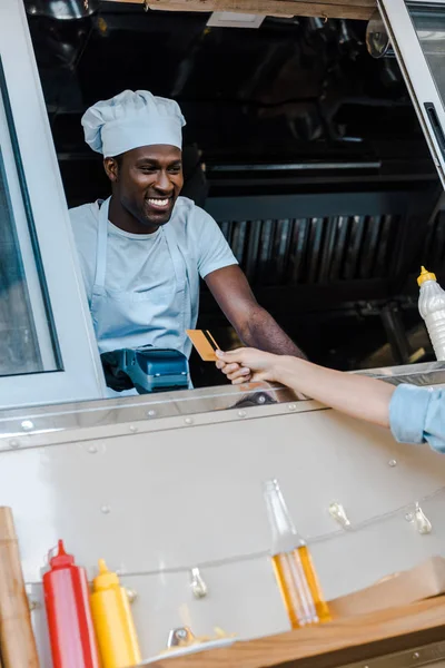 Обрезанный вид женщины, держащей кредитную карту при оплате в фургоне с едой возле африканского американского мужчины — стоковое фото