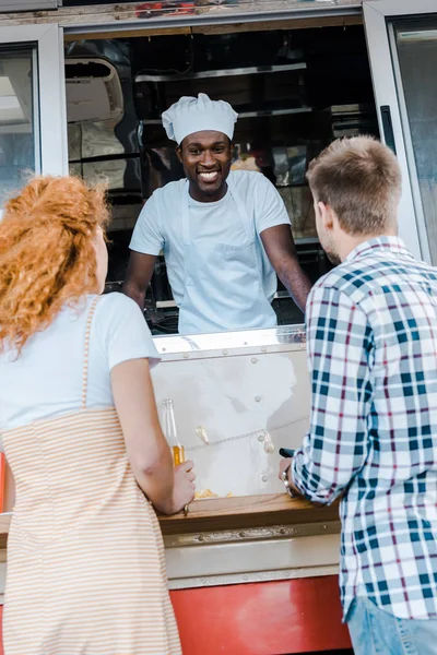 Vista trasera de los clientes cerca de hombre americano africano alegre en camión de coche - foto de stock