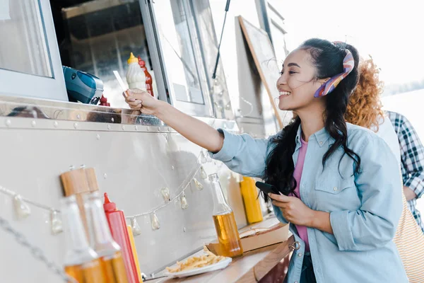 Вибірковий фокус щасливої азіатської дівчини, що тримає кредитну картку поблизу клієнтів і продовольчої вантажівки — стокове фото
