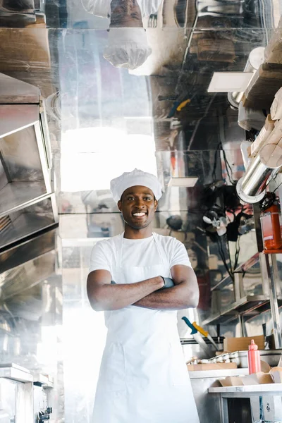 Alegre afroamericano chef de pie con brazos cruzados en camión de comida - foto de stock