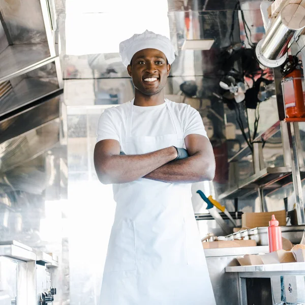 Chef afroamericano positivo de pie con los brazos cruzados en camión de comida - foto de stock