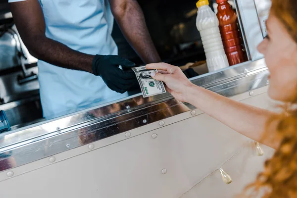 Foco seletivo da menina ruiva dando dinheiro ao homem americano africano no caminhão de alimentos — Fotografia de Stock