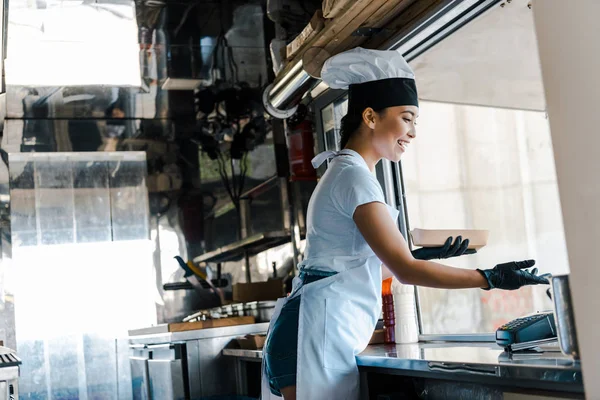 Щаслива азіатська жінка в латексних рукавичках тримає картонну тарілку в харчовій машині — стокове фото