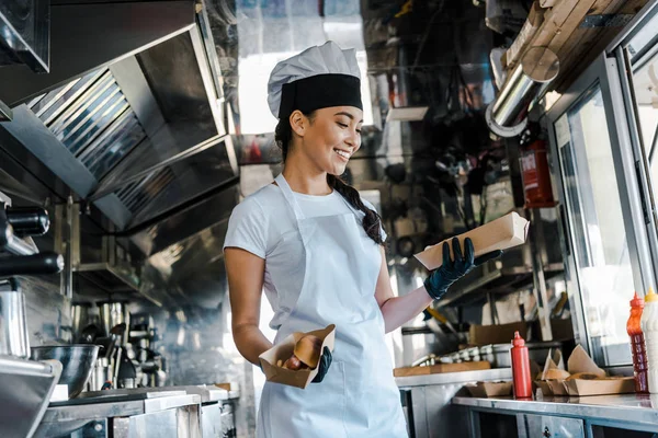 Feliz asiático chef no chapéu segurando placas de papelão no caminhão de alimentos — Stock Photo