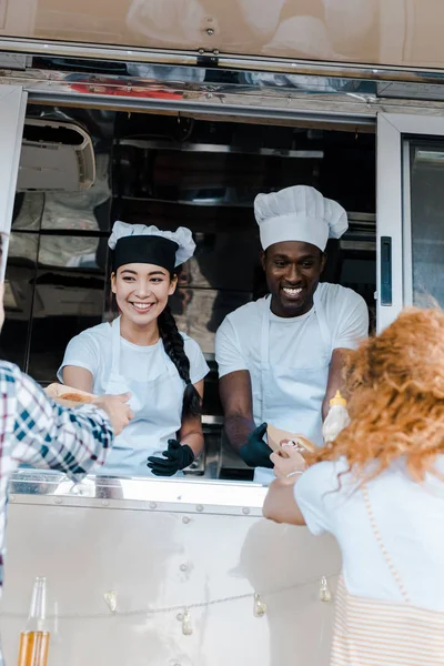 Selective focus of smiling multicultural chefs giving carton plates with food to customers — Stock Photo