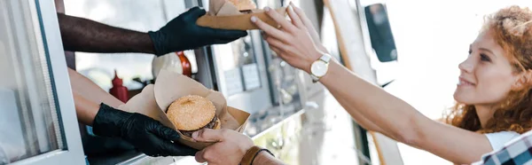 Panoramic shot of multicultural chefs giving carton plates with food to happy customers — Stock Photo