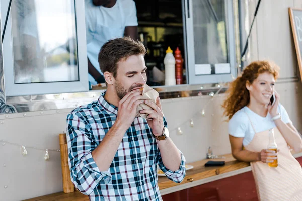 Messa a fuoco selettiva di bell'uomo mangiare gustoso hamburger vicino al camion cibo — Foto stock