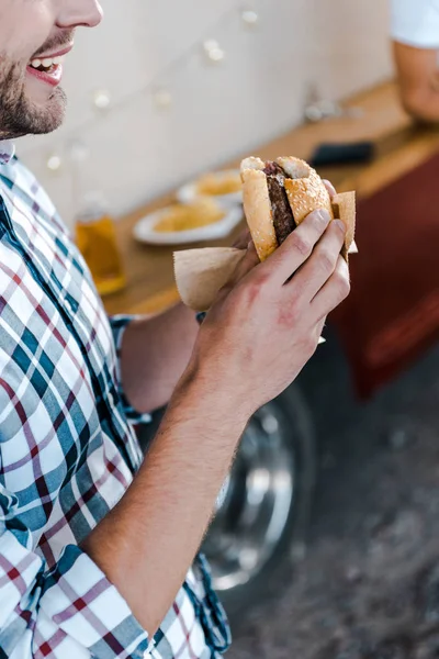 Vista cortada de homem feliz segurando hambúrguer saboroso — Fotografia de Stock