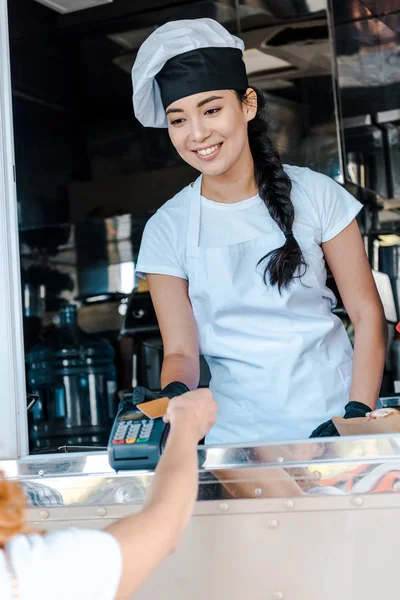 Selective focus of asian woman smiling near customer paying by credit card — Stock Photo