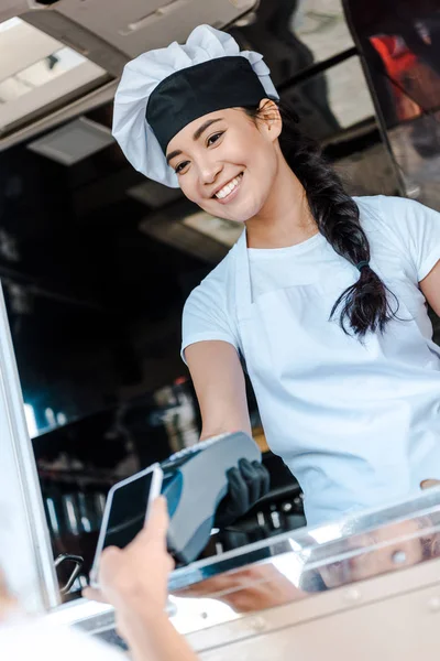 Vue recadrée de femme payer avec smartphone près asiatique fille dans food truck — Photo de stock