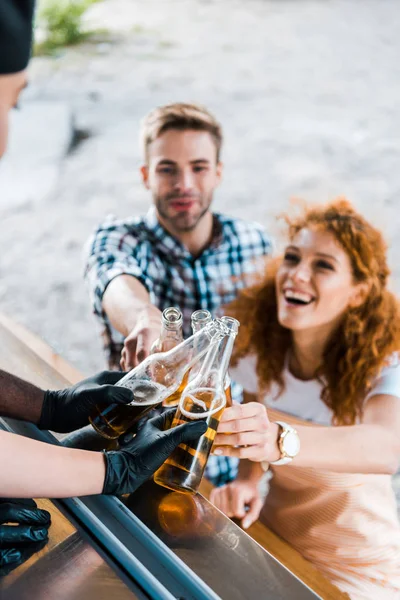 Selective focus of multicultural chefs toasting with bottles of beer near customers — Stock Photo