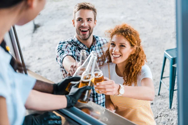Selective focus of multicultural chefs toasting with bottles of beer near happy customers — Stock Photo
