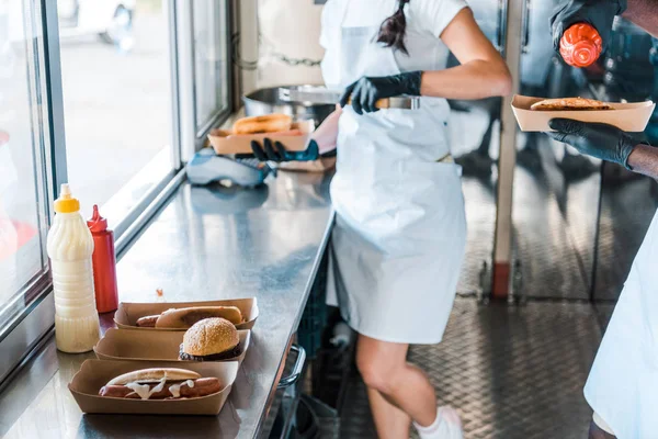 Cropped view of girl and african american man holding street food in food truck — Stock Photo