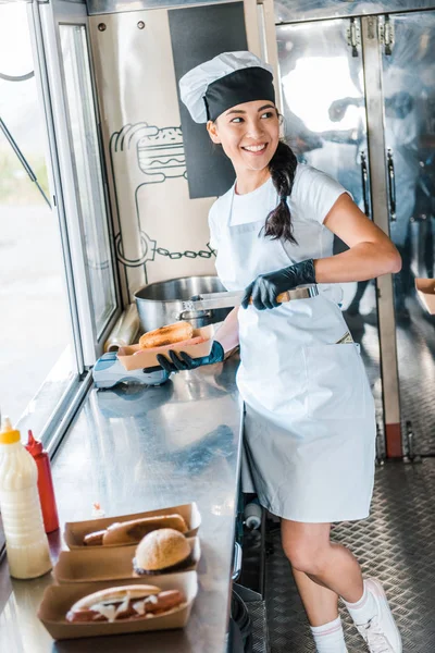 Heureux asiatique fille tenant carton plaque tout en mettant hot dog — Photo de stock