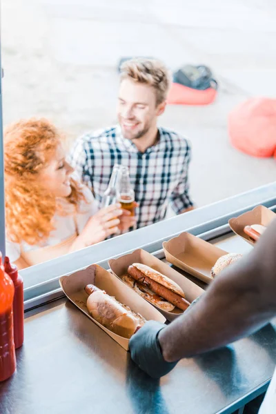 Cropped view of african american chef near hot dogs and customers — Stock Photo