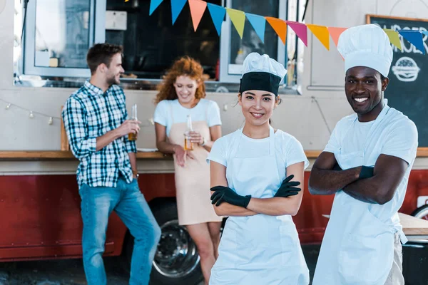 Selective focus of cheerful multicultural chefs smiling near food truck and customers — Stock Photo