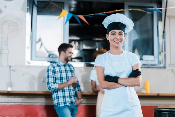 Selettivo fuoco di allegro asiatico chef standing con braccia incrociate vicino cibo camion e clienti — Foto stock