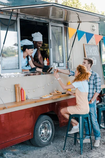 Customers clinking beer with multicultural chefs in food truck — Stock Photo