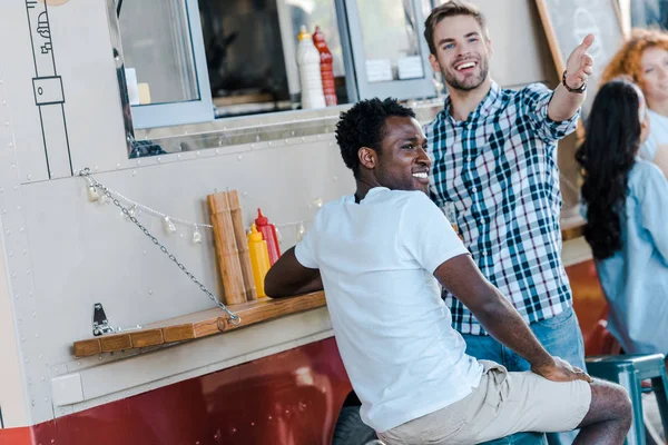 Enfoque selectivo de los hombres guapos gesto cerca de amigo afroamericano y camión de comida - foto de stock