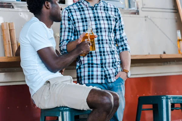 Vista cortada de homens multiculturais clinking garrafas com cerveja perto de caminhão de alimentos — Fotografia de Stock