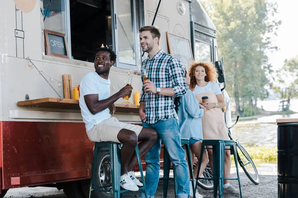 Cheerful and young multicultural people near food truck — Stock Photo