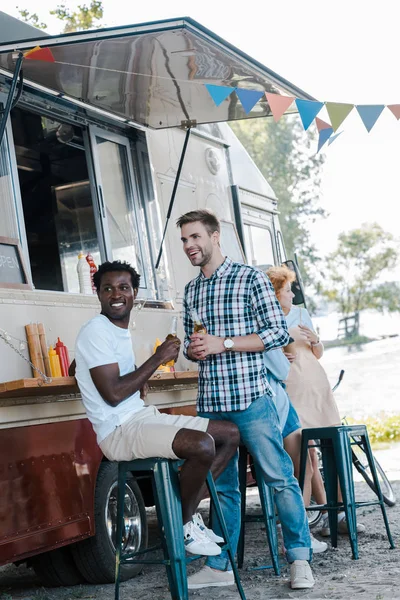 Heureux hommes multiculturels près de camion alimentaire et les femmes — Photo de stock