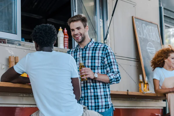 Selektiver Fokus eines gutaussehenden Mannes, der seinen afrikanisch-amerikanischen Freund anschaut und Bier in der Hand hält — Stockfoto