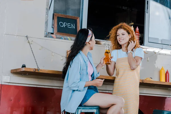 Happy multicultural girls clinking bottles with beer near food truck — Stock Photo
