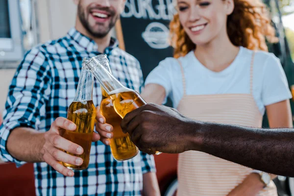 Cropped view of happy multicultural men clinking with redhead woman near food truck — Stock Photo