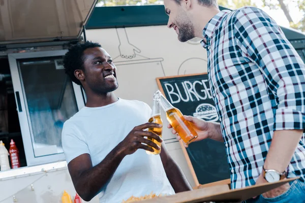 Low angle view of happy multicultural men toasting bottles of beer — Stock Photo