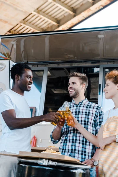 Messa a fuoco selettiva di uomini multiculturali clinking bottiglie di birra con felice rossa donna vicino camion cibo — Foto stock