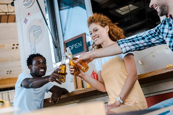 Bonito multicultural homens clinking garrafas de cerveja com atraente ruiva mulher perto de comida caminhão — Fotografia de Stock