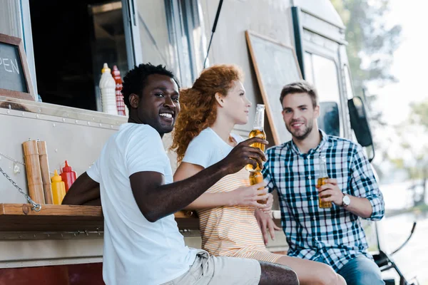 Enfoque selectivo del hombre afroamericano guapo sosteniendo botella de cerveza cerca de amigos - foto de stock