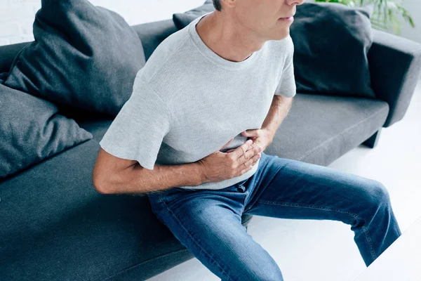 Vista recortada del hombre en camiseta con dolor de estómago en el apartamento - foto de stock