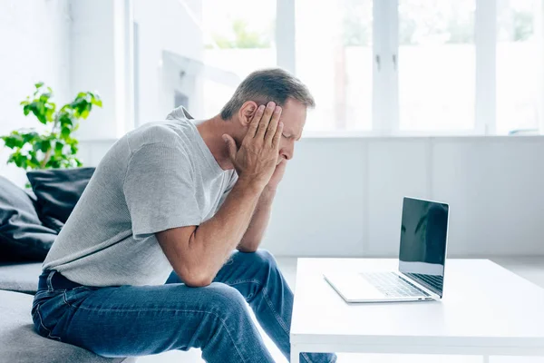 Vue latérale du bel homme en t-shirt avec les yeux fermés touchant la tête dans l'appartement — Photo de stock