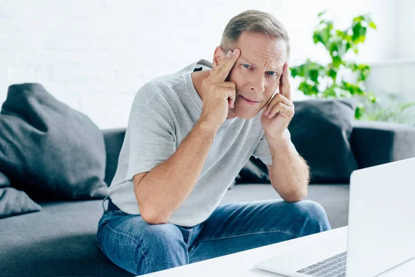 Bel homme en t-shirt avec les yeux fermés touchant la tête dans l'appartement — Photo de stock