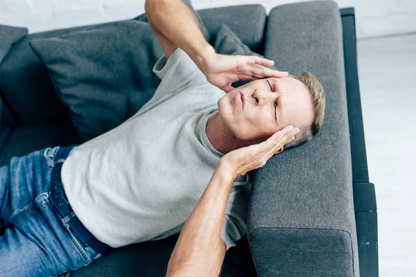 Hombre guapo en camiseta con los ojos cerrados tocando la cabeza en el apartamento - foto de stock